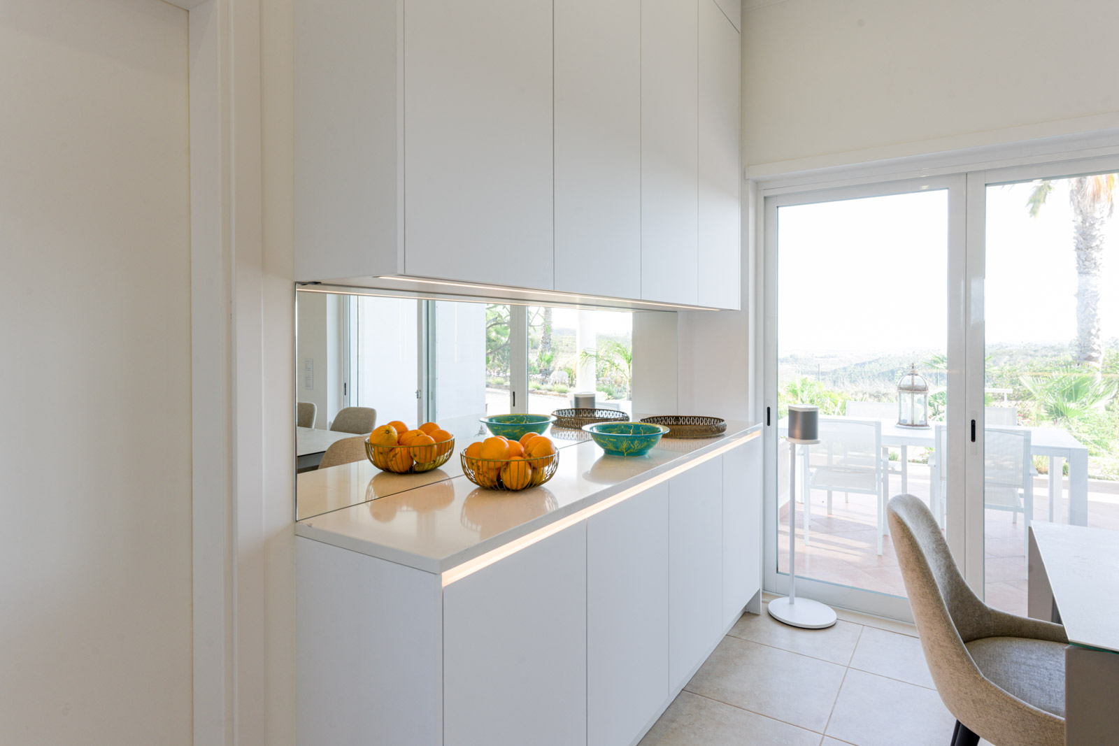 Cozinha branca com bancada em Silestone Calacatta Gold e forro de parede em espelho.